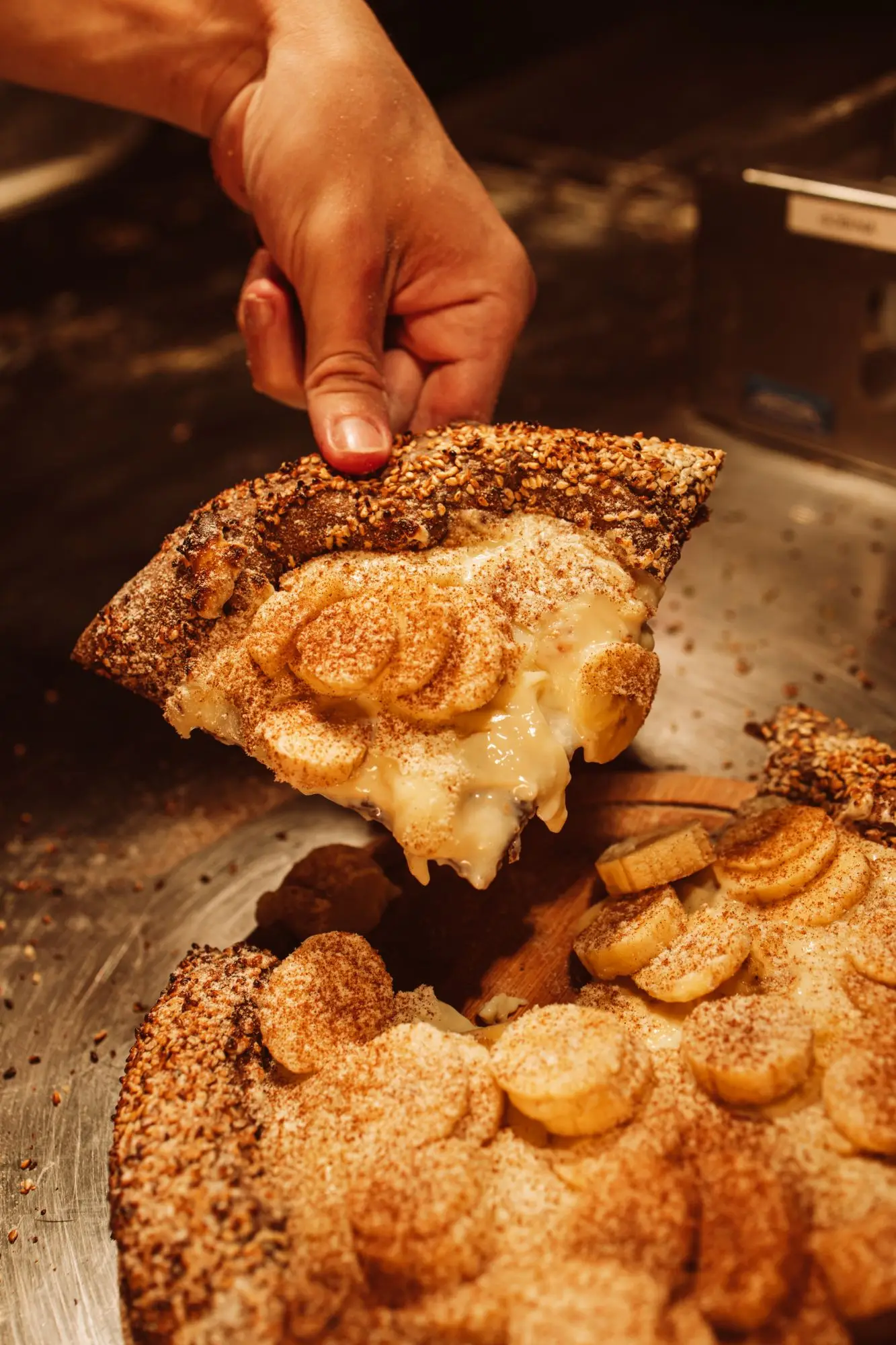 Fatia da pizza doce de banoffee com a borda de gergelim sendo levantada