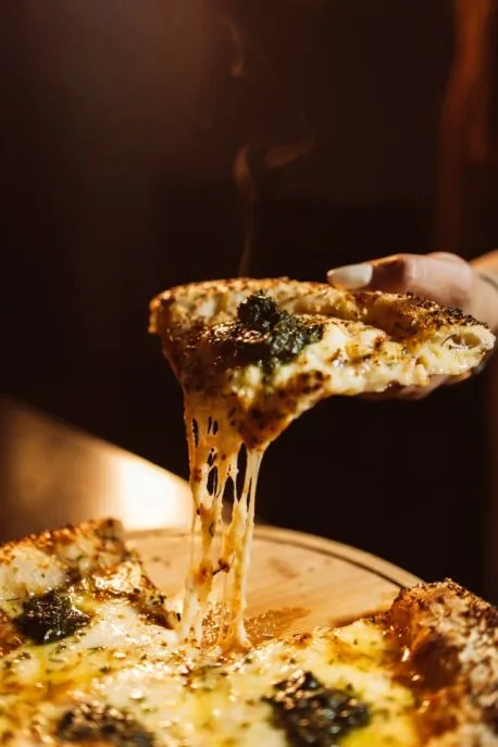 Fatia de pizza sendo levantada, com o queijo esticando e vapor subindo